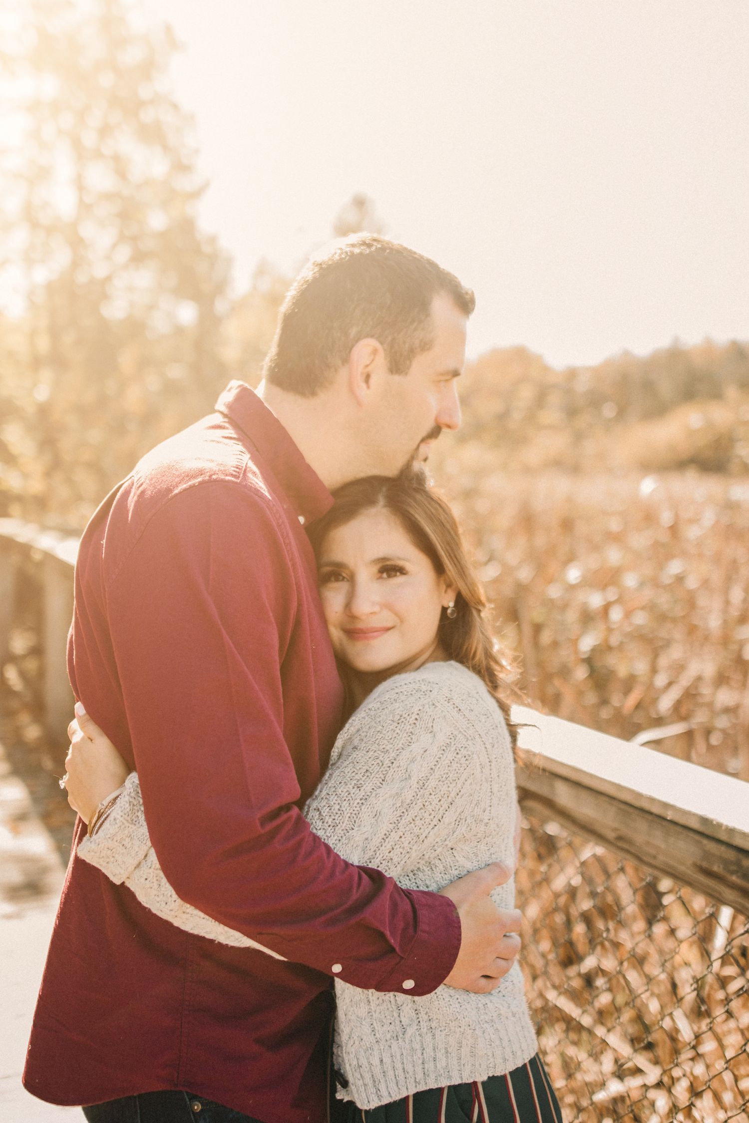 A couple in casual autumn attire shares a tender embrace in a sunlit field.