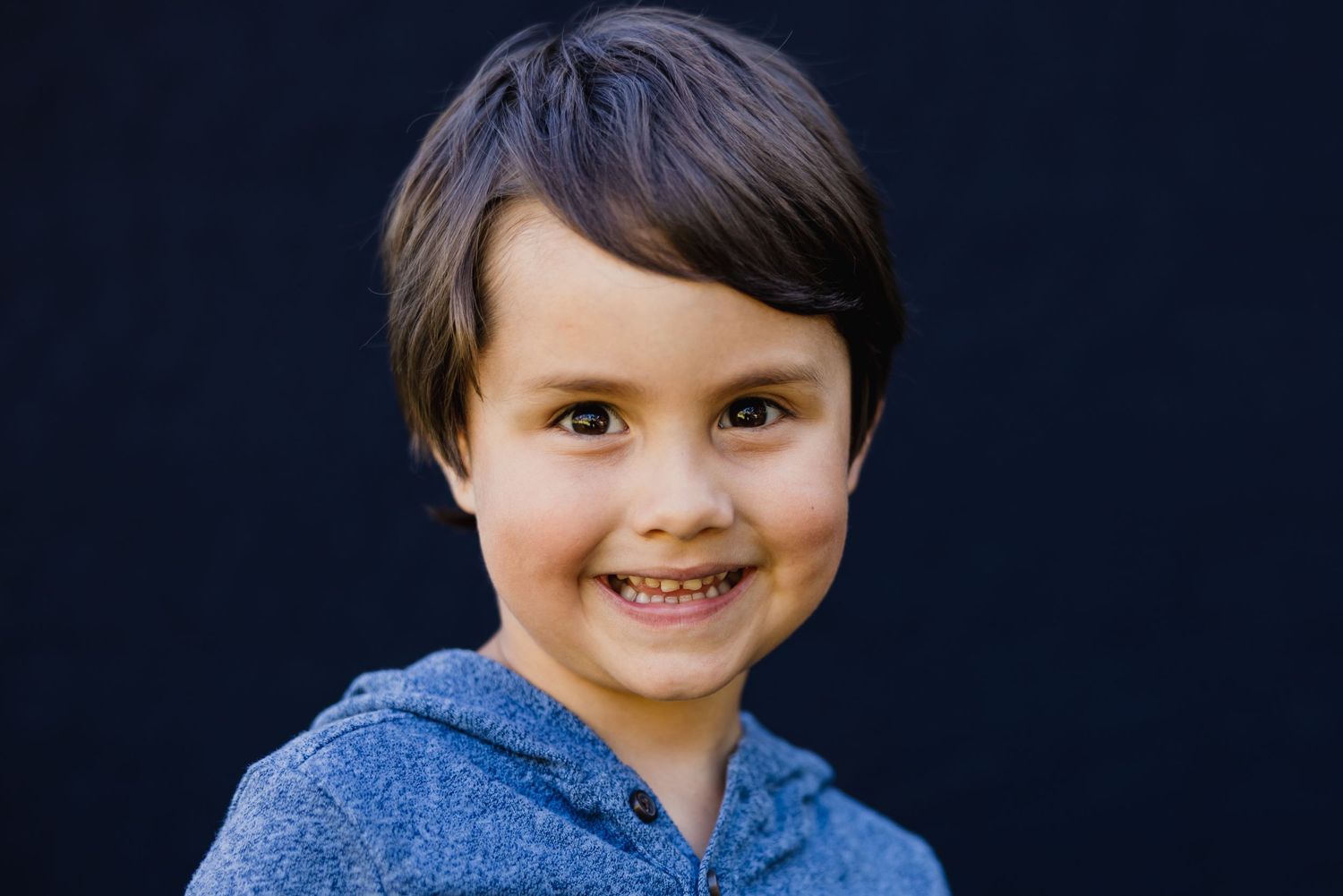 A cheerful portrait of a young person wearing a blue hoodie against a dark background.