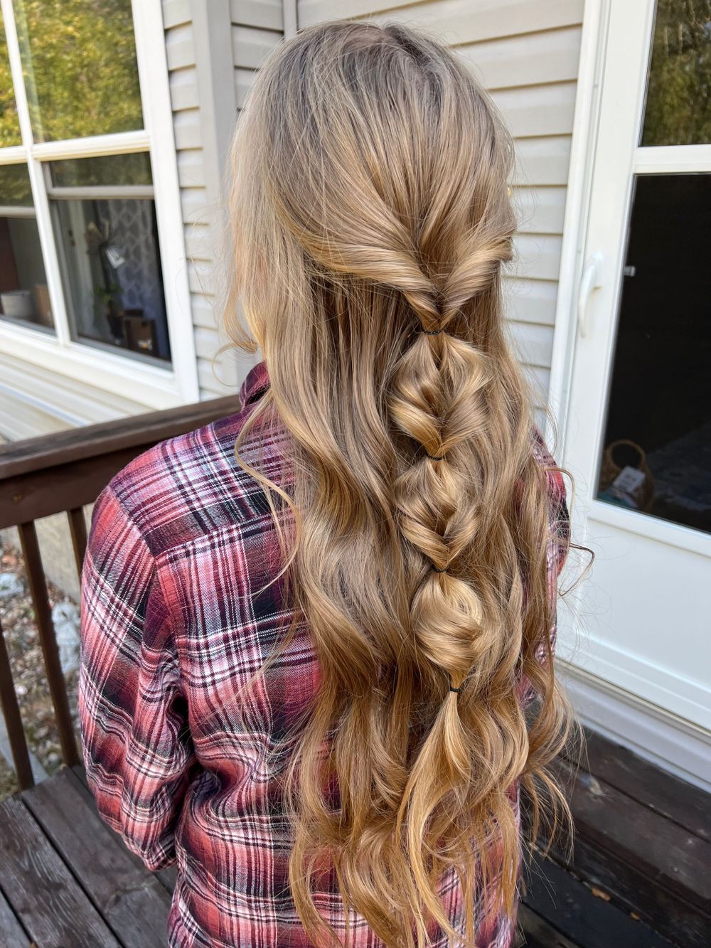 Detailed shots of long braided hairstyle with pink plaid shirt against white house siding.