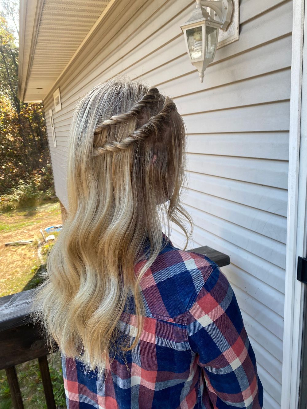 Blonde hair styled in a casual updo wearing a plaid flannel shirt against white siding.
