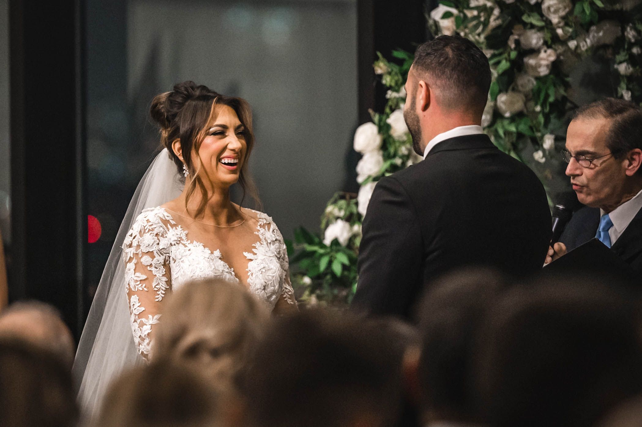 Wedding ceremony with couple exchanging vows under floral decor with guests watching.