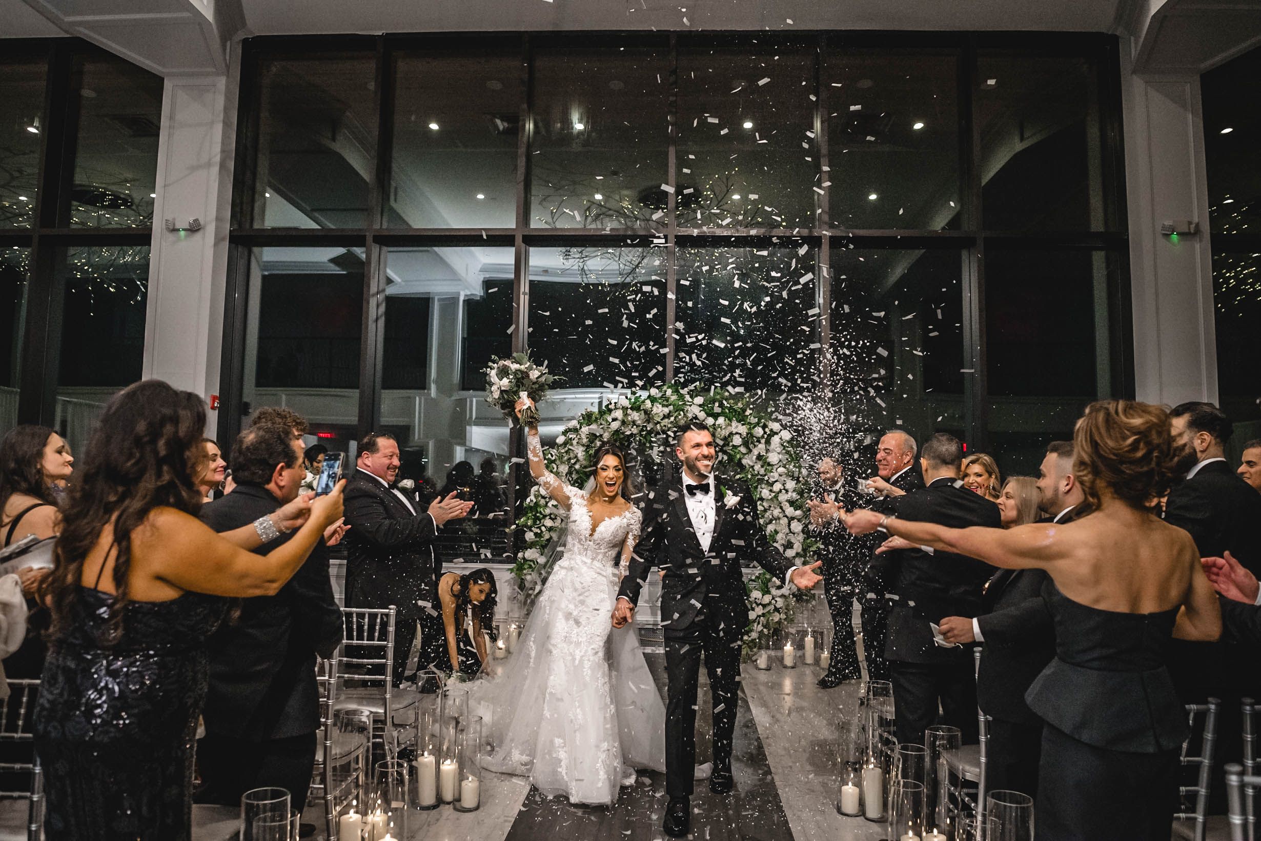 Newlyweds walk down aisle while guests throw confetti in celebration.