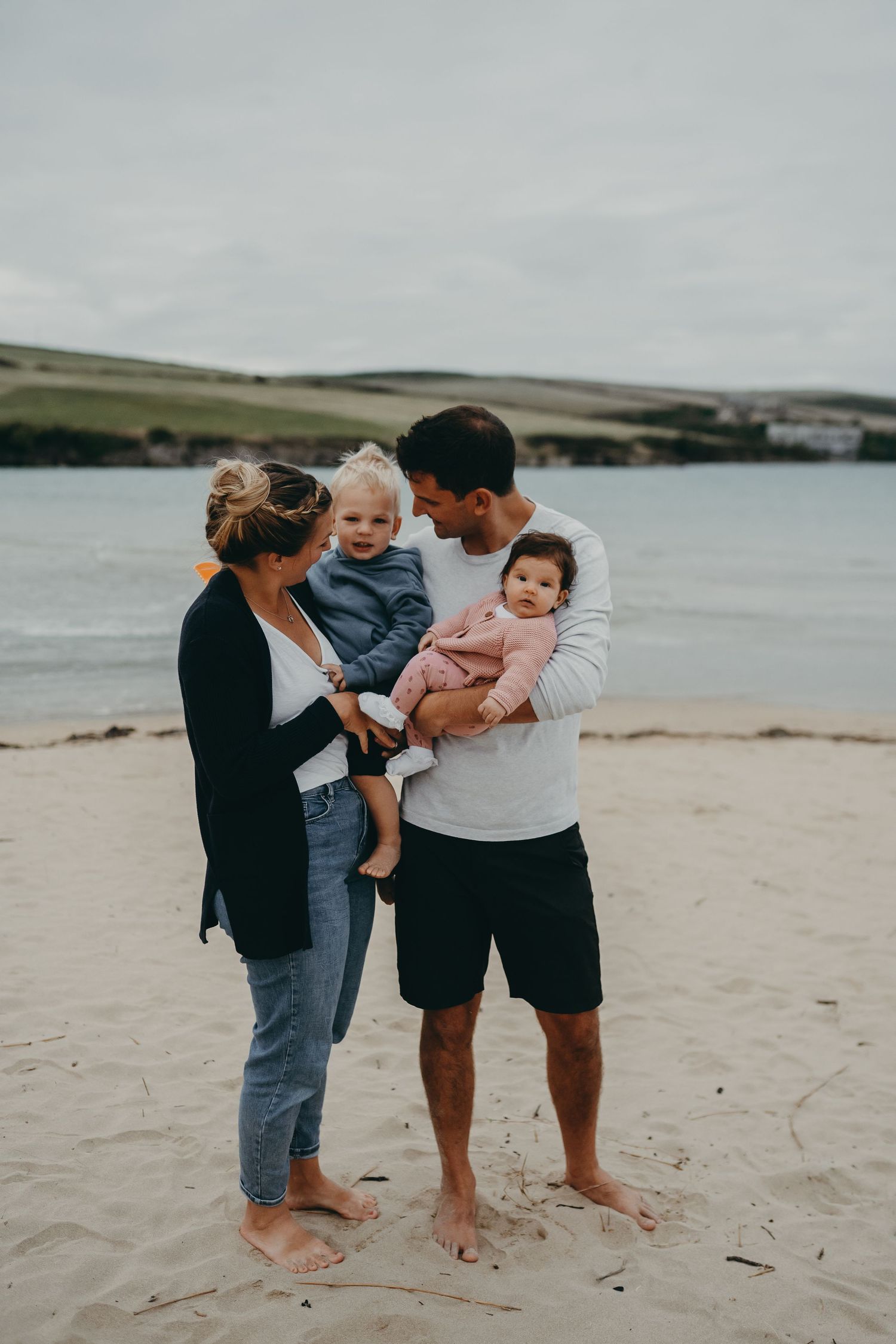 A family spending time together on a sandy beach with water and hills in the background.
