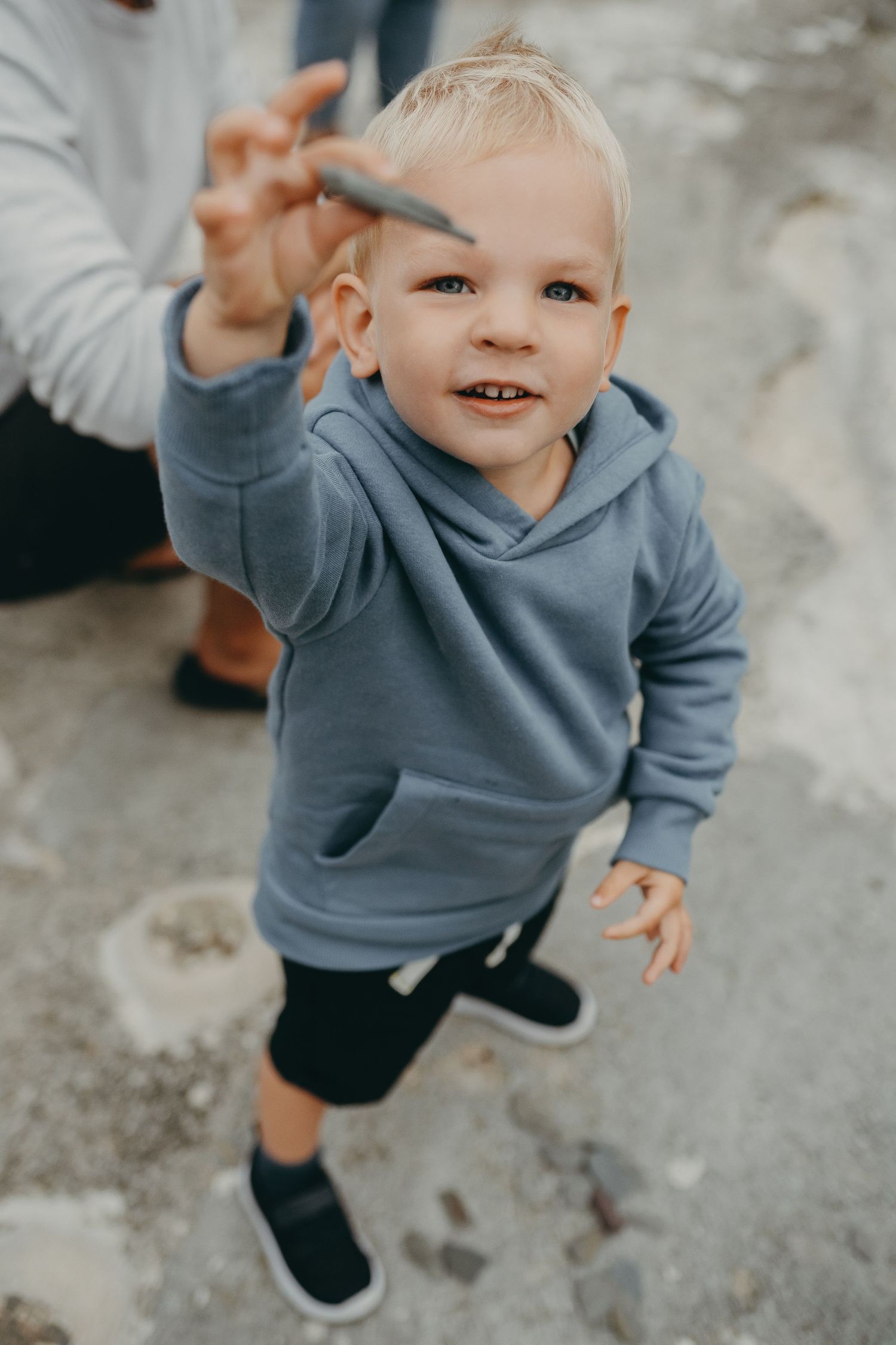 A young child in a blue hoodie smiles playfully while reaching toward the camera.