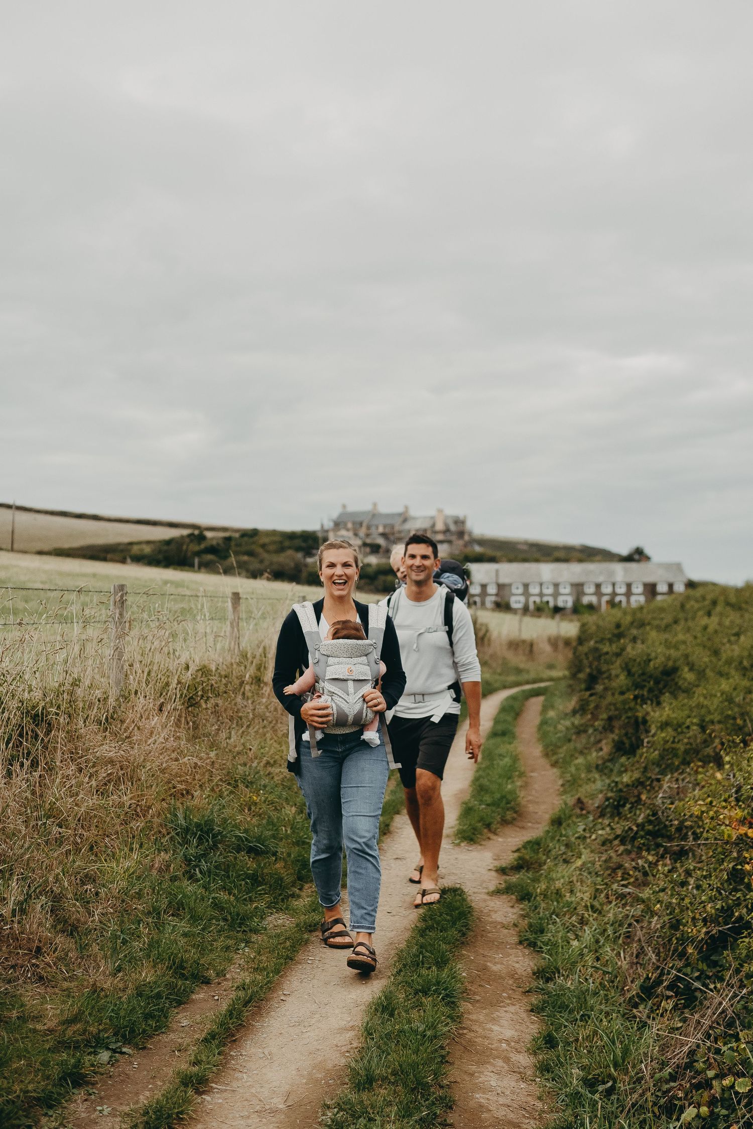 Hikers walking along a coastal trail with rolling hills and ocean views in the background.