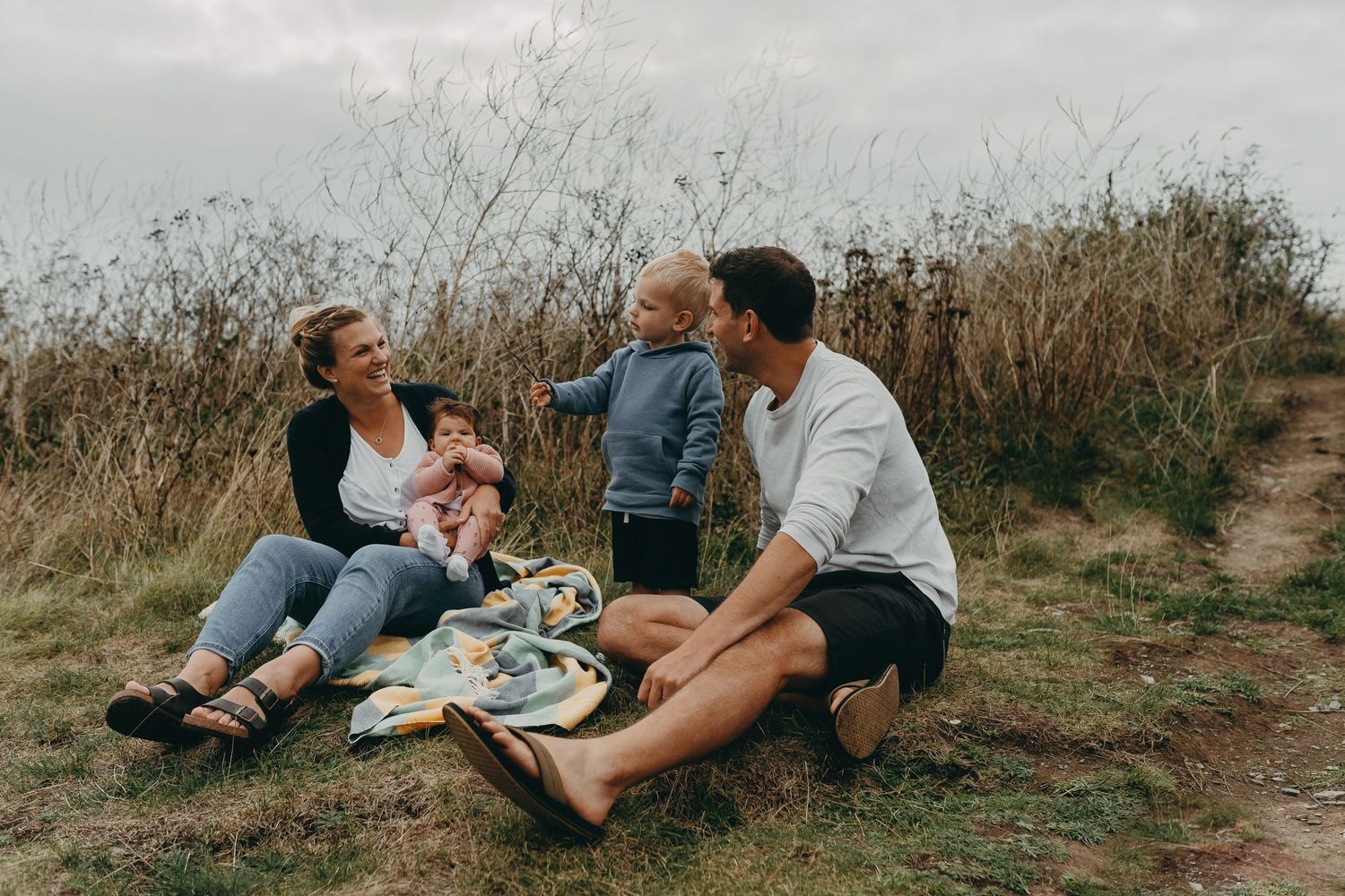 A family enjoying a relaxing picnic together on a grassy hill during an overcast day.