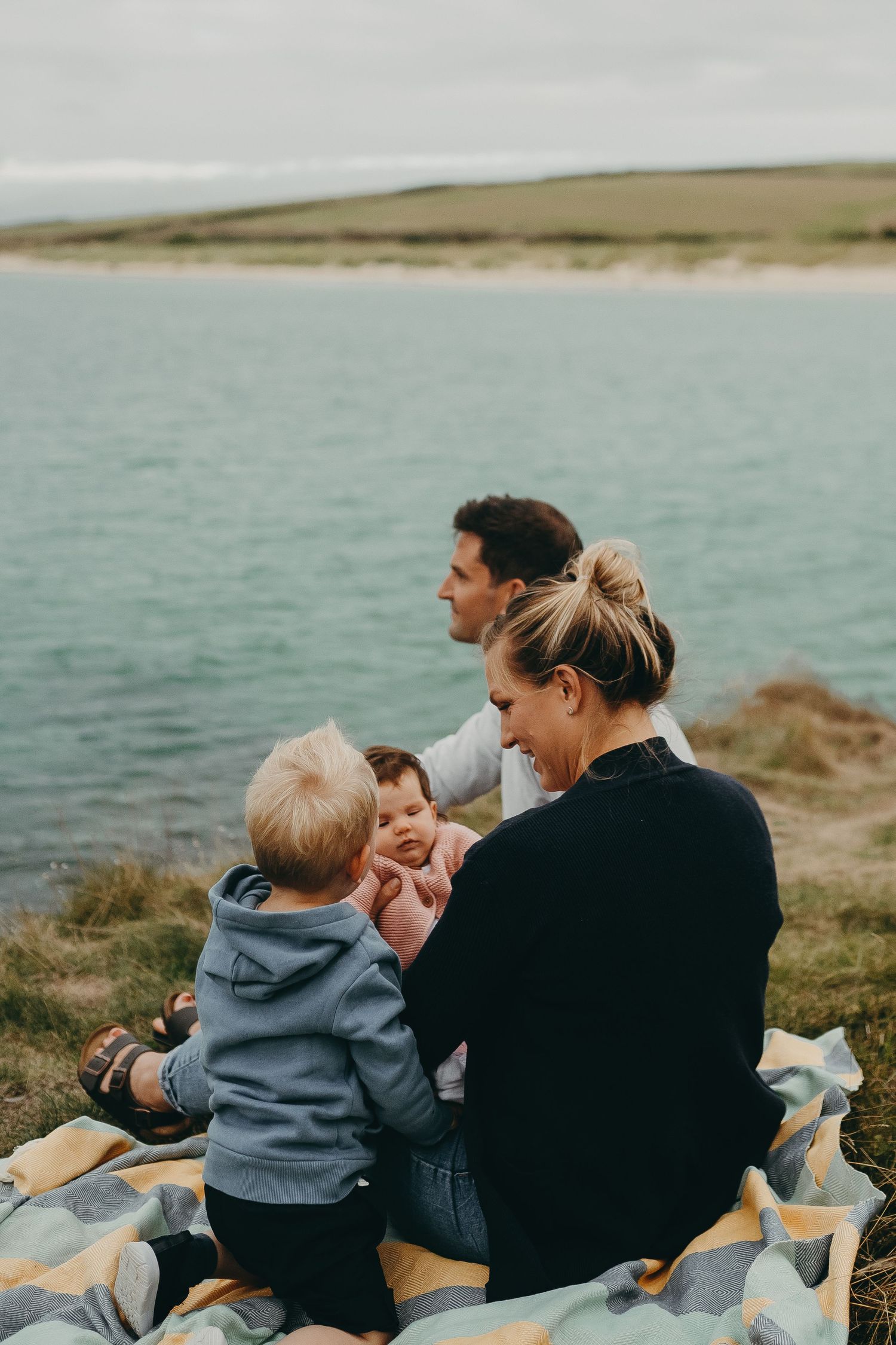 A family shares a joyful moment while sitting on a blanket overlooking the coastline.