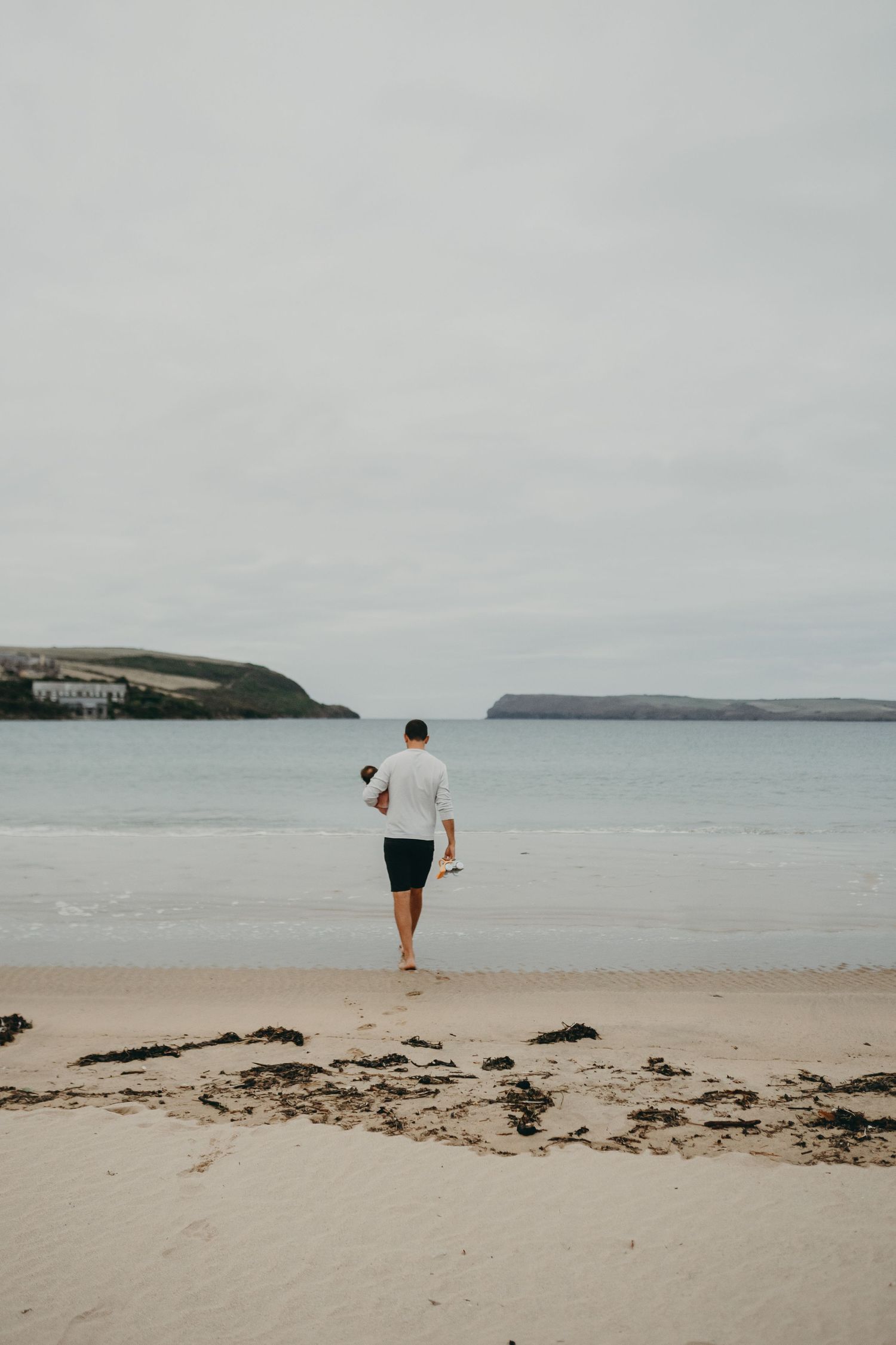A lone figure walks along an empty beach with cliffs and ocean in the background.