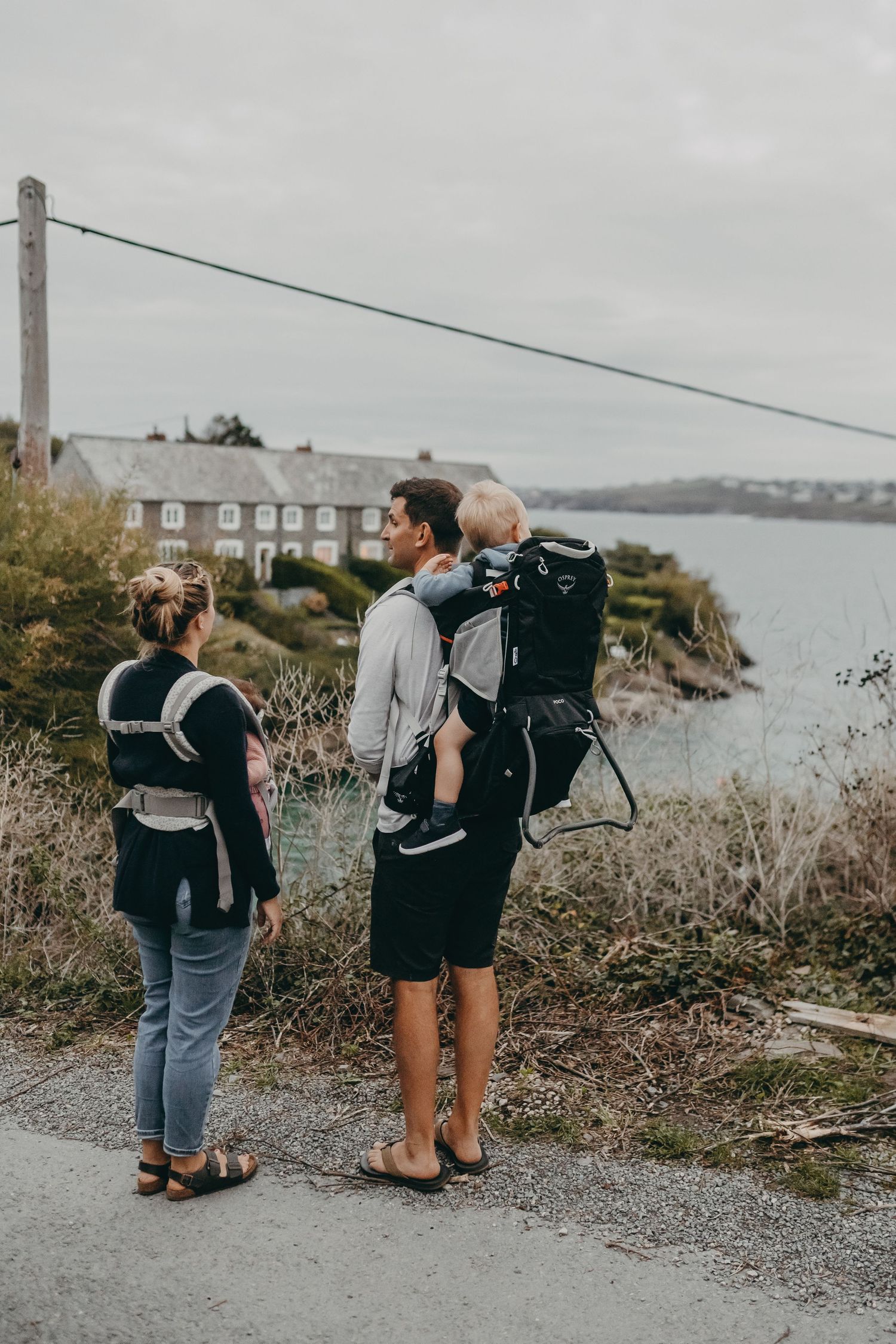 Group hiking along coastal path with backpacks overlooking seaside houses and water.