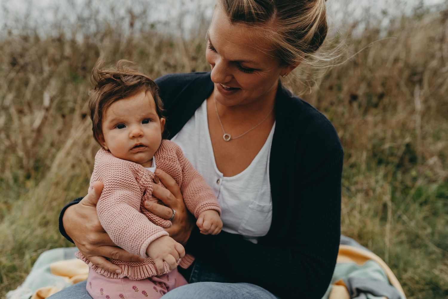 An intimate outdoor portrait of parent and baby in matching pink outfits against a natural backdrop.