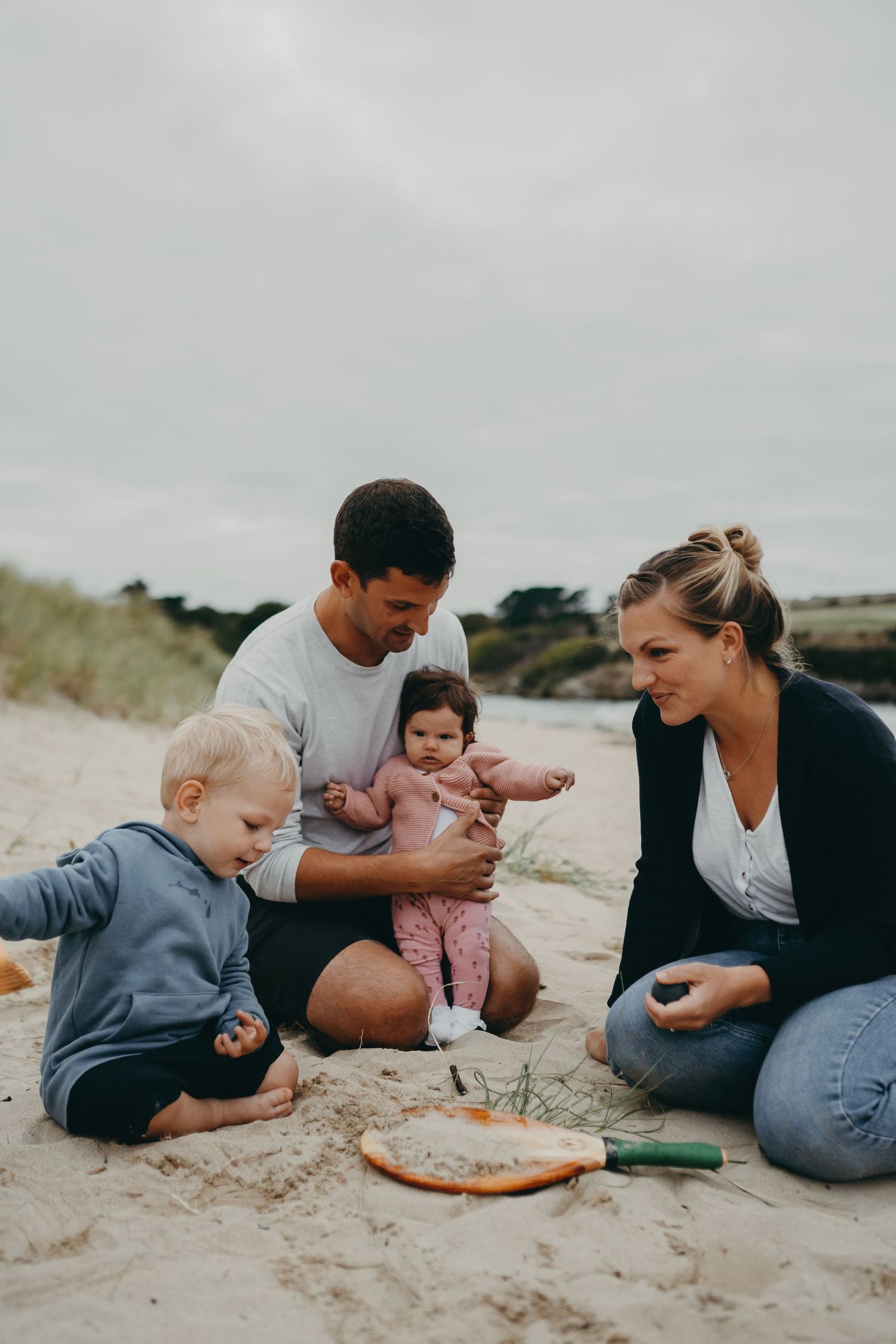 A family sitting together on the beach sand sharing snacks and quality time.