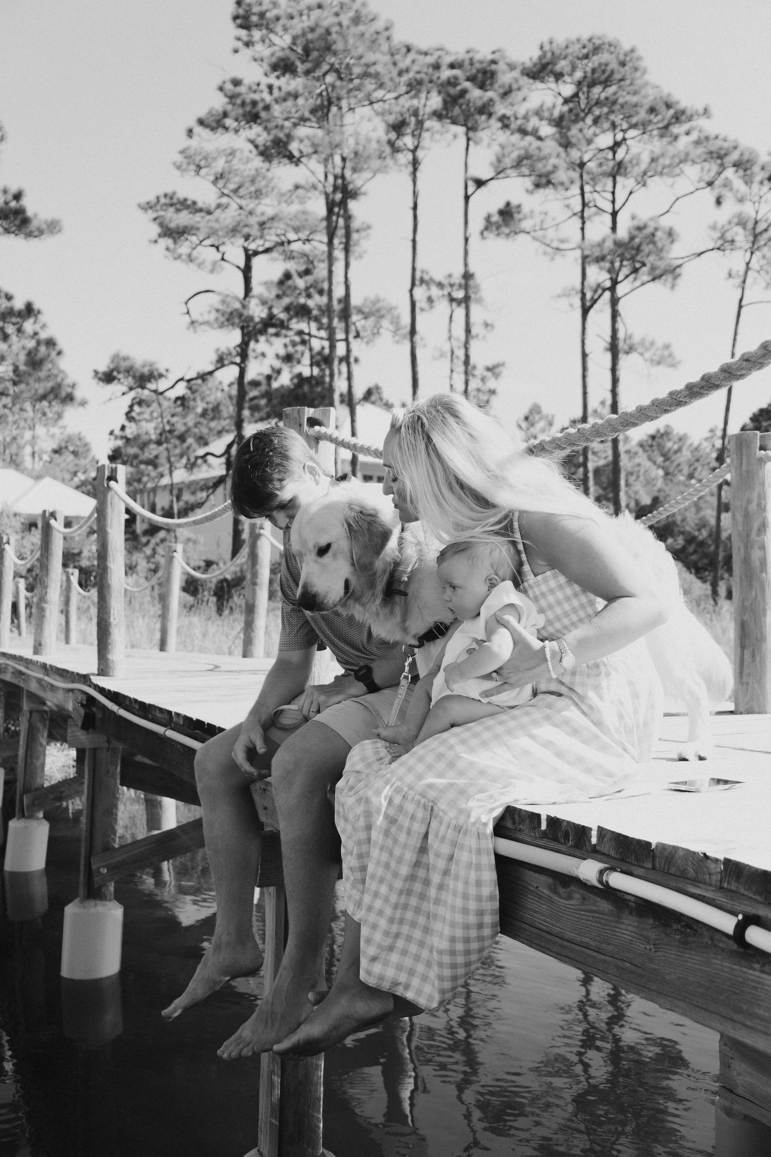 Black and white sequence of playful moments on a wooden dock by pine trees.