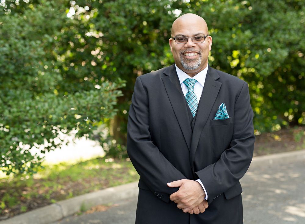 Professional in dark suit with turquoise tie standing outdoors.