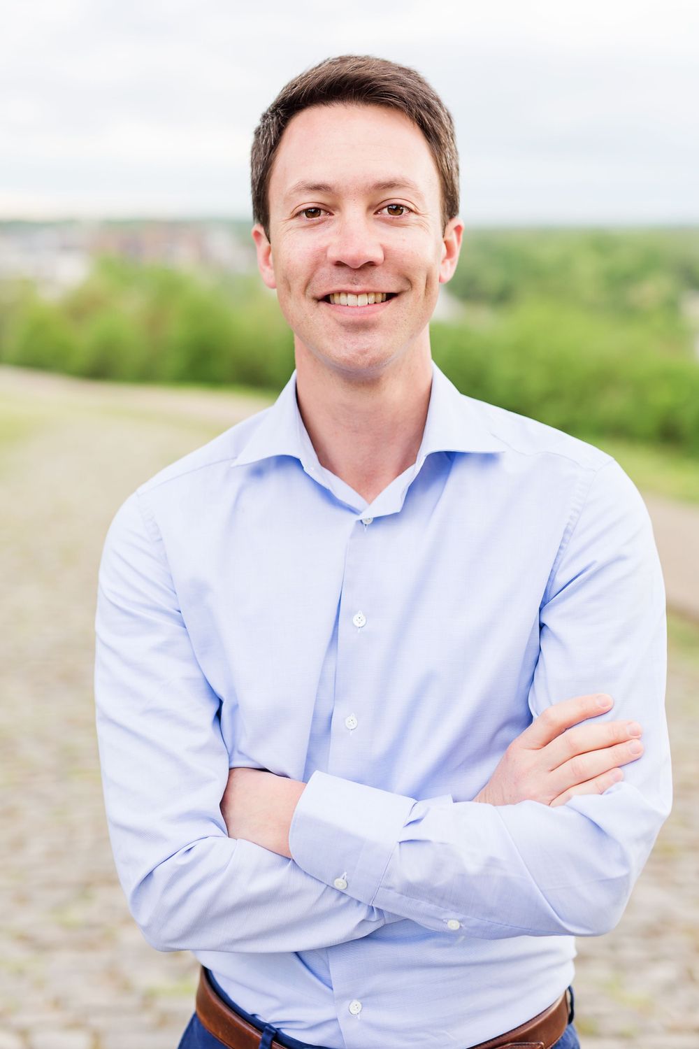 Casual outdoor portrait of person in light blue button-down shirt with arms crossed.