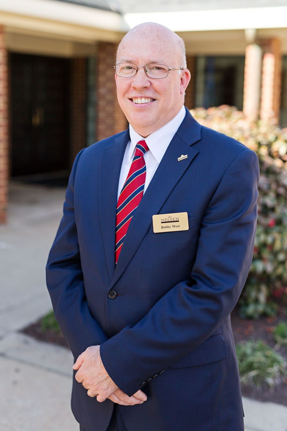 Professional portrait of person in navy suit with red striped tie wearing name tag.