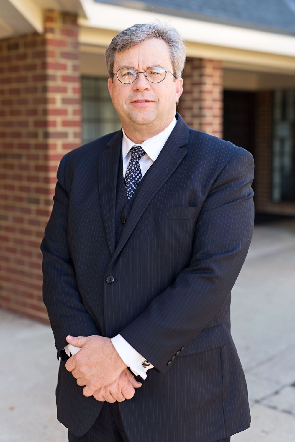 Professional business portrait of person in dark pinstriped suit and tie against brick building.