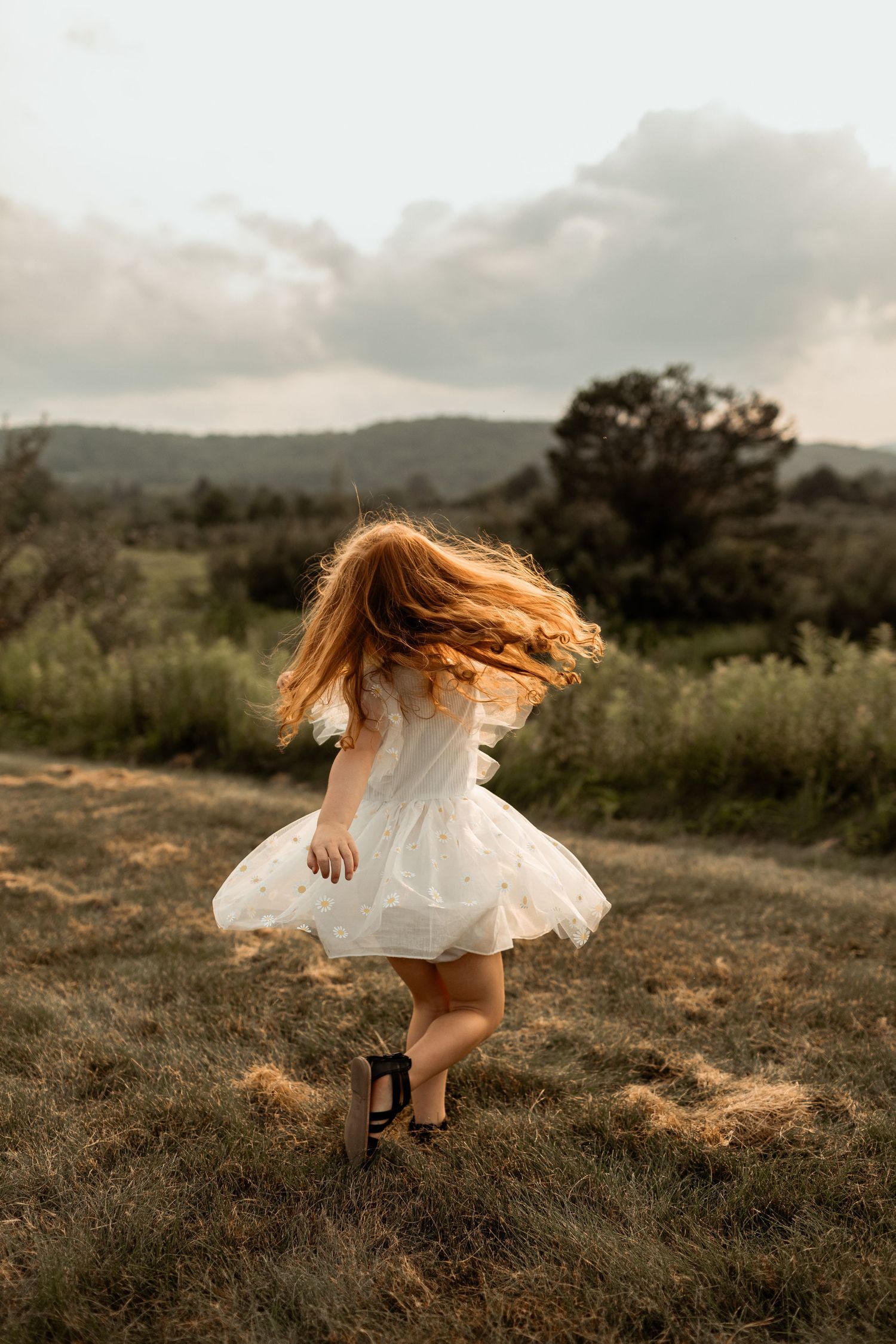 A girl in a white dress twirling in a field during golden hour.