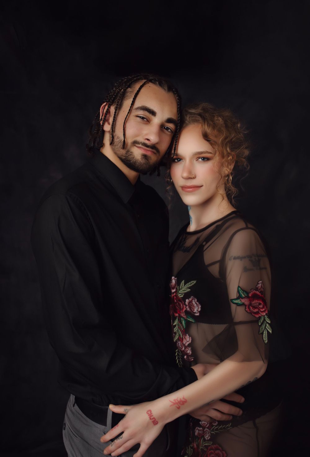 Romantic couple portrait with floral sheer dress against dark background.