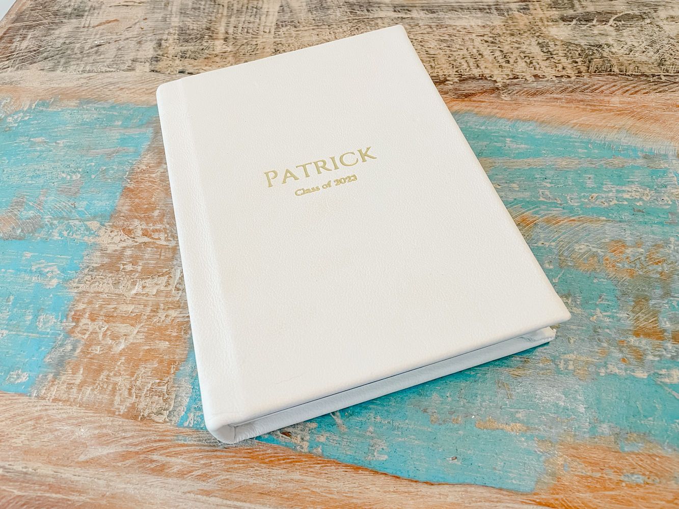 White photography album boxes displayed on a rustic turquoise wooden surface.