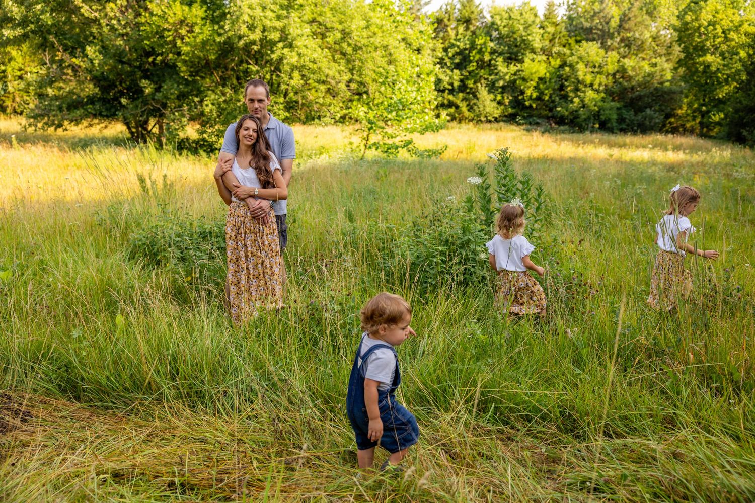 Family playing together in tall summer grass field during golden hour.