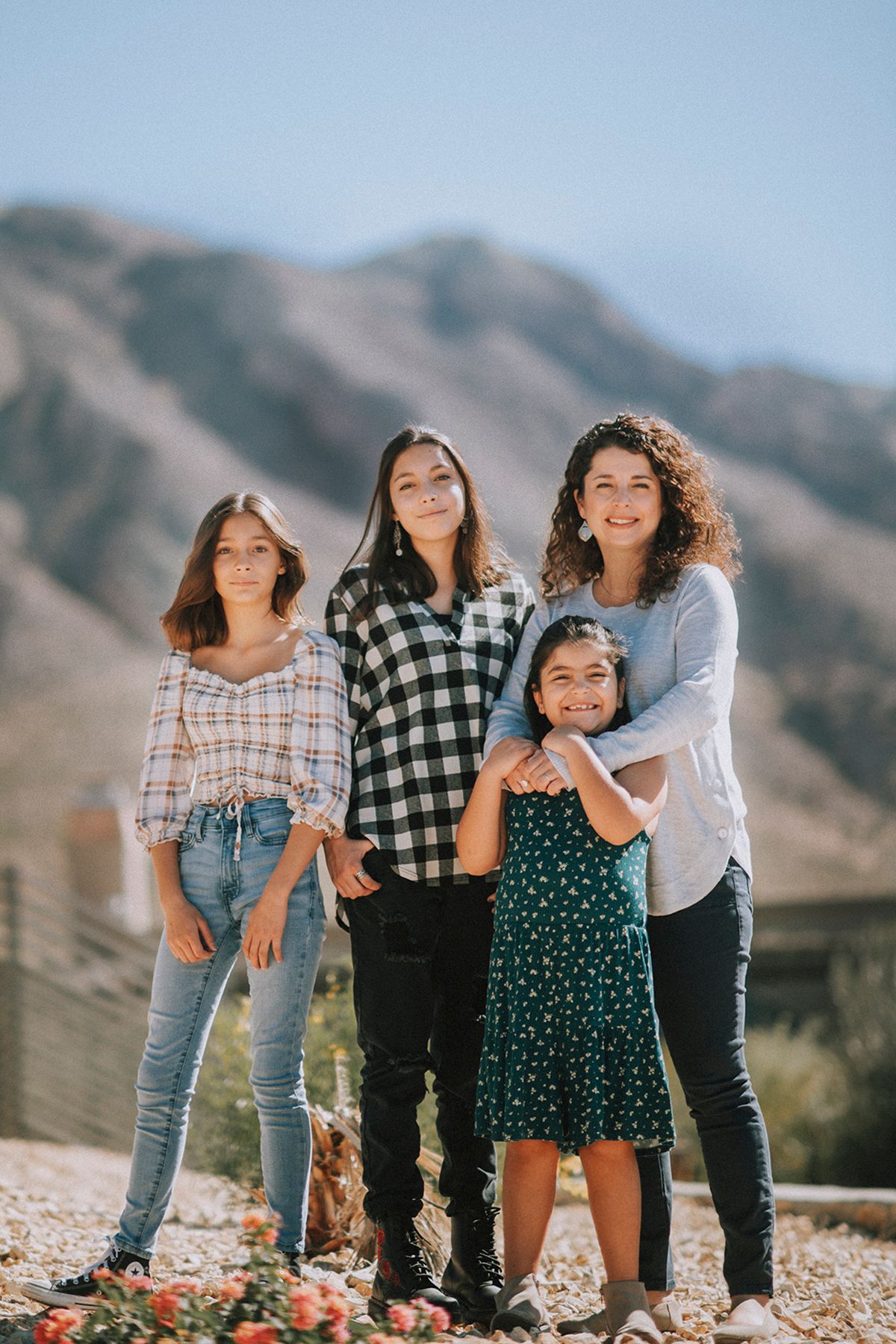 A group stands together outdoors smiling against a mountain backdrop wearing casual clothing.
