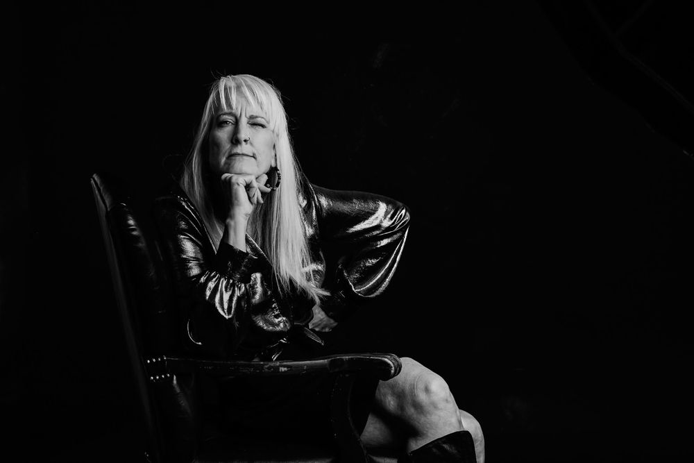 Dramatic black and white portrait of a person with silver hair against dark background.