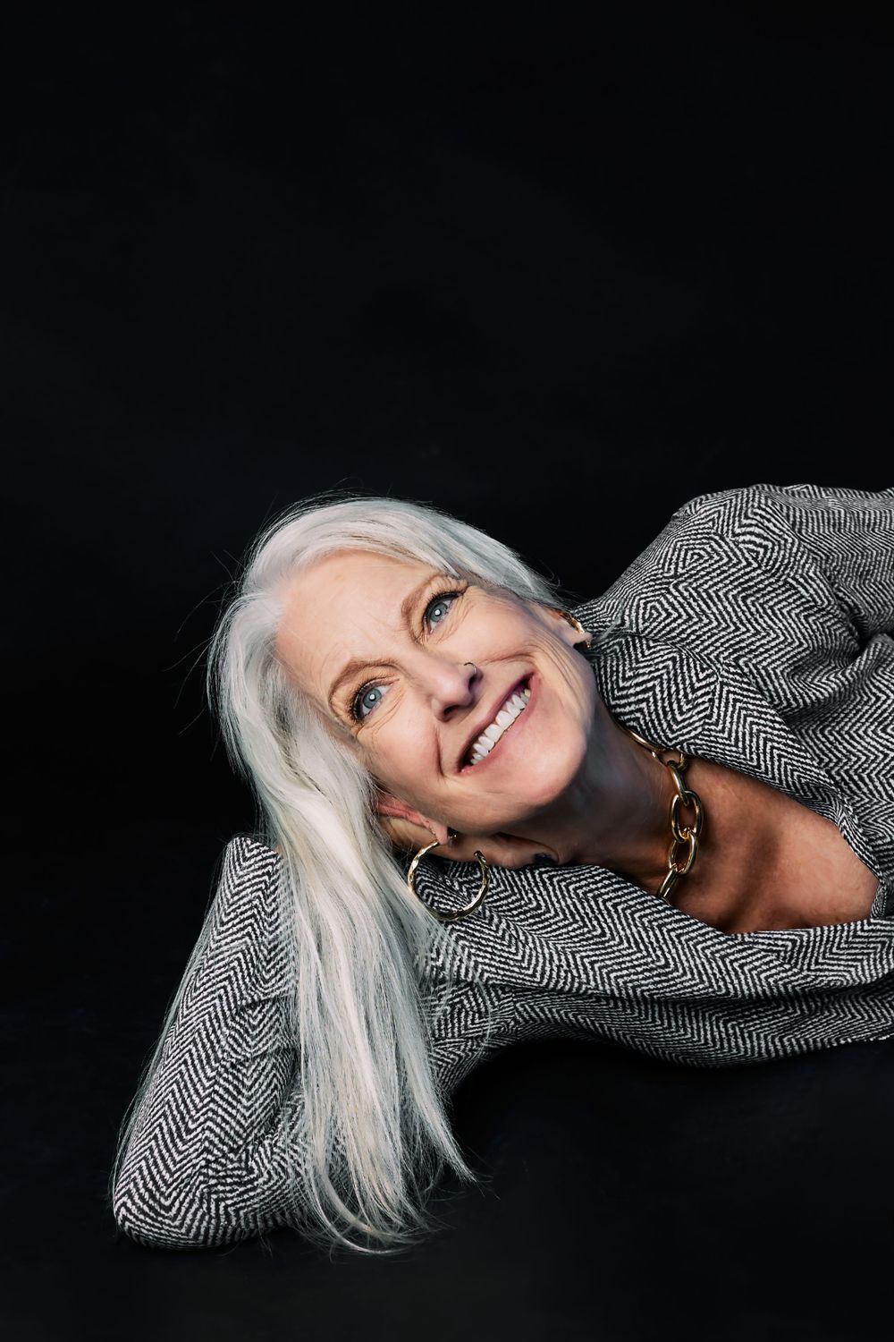 Creative portrait series showing person with silver hair in patterned jacket lying down against black background.