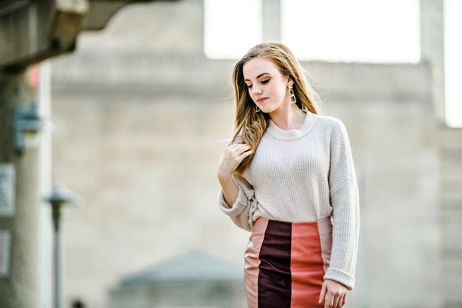 Female senior in casual grey sweater and rust-colored skirt standing outdoors against concrete wall by Stephanie Coulter Photography