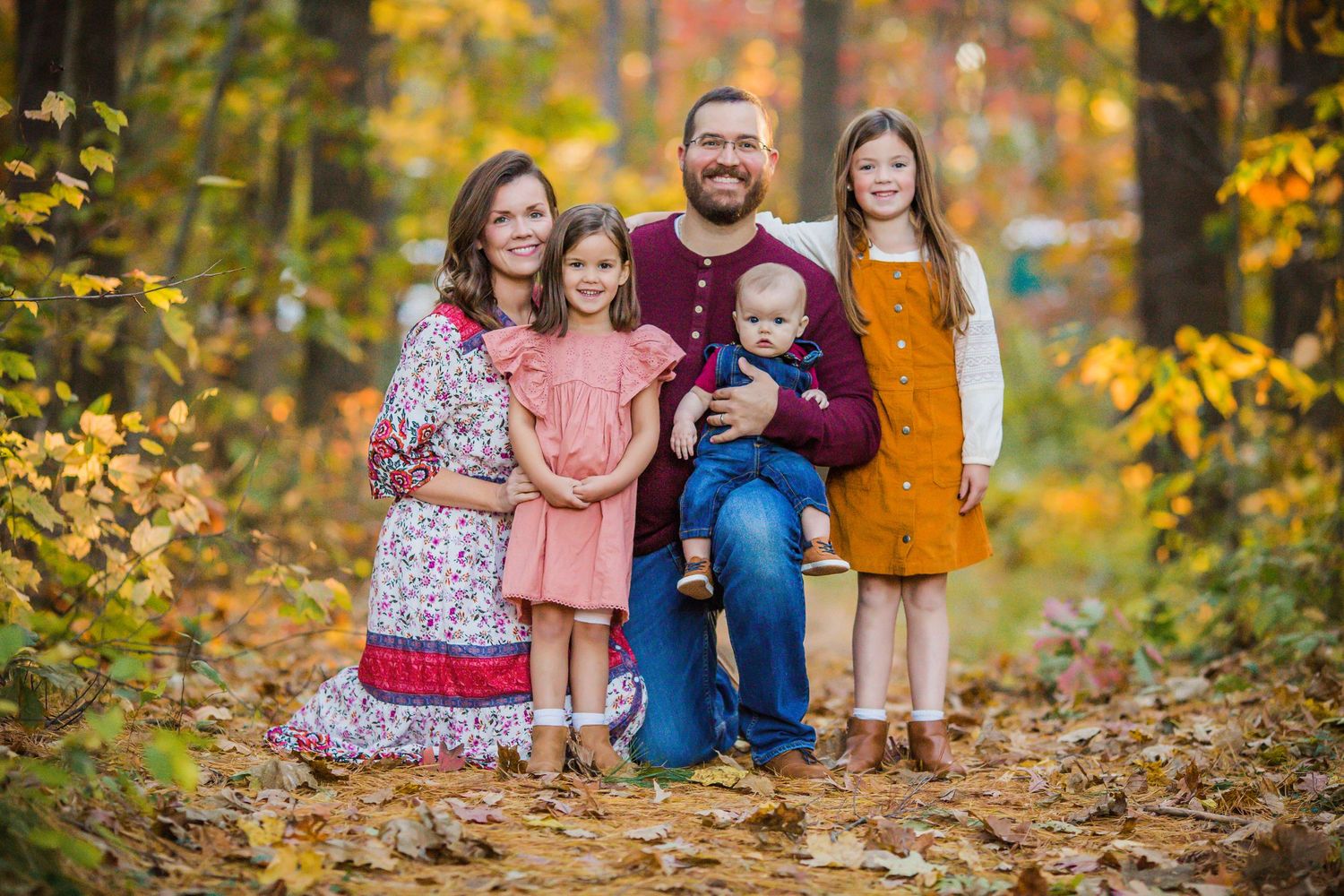 Family of five posing together among colorful autumn foliage in a forest setting.