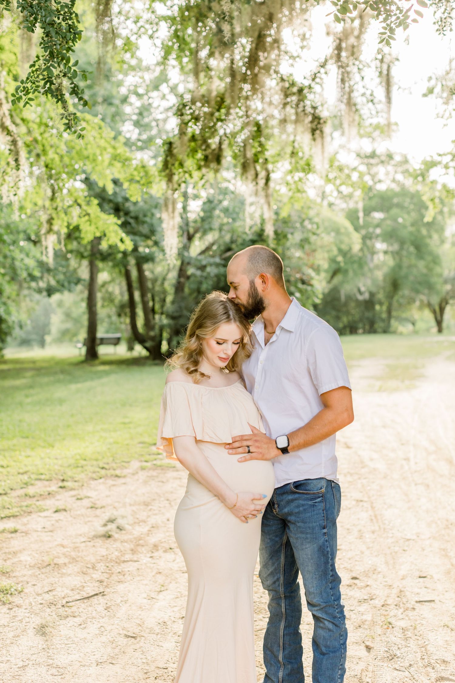 An intimate maternity portrait under Spanish moss trees with soft natural lighting.