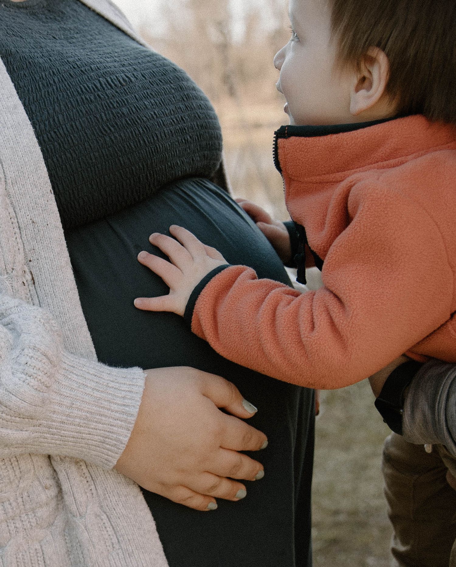 Close-up of small hands touching pregnant belly in warm winter clothing.