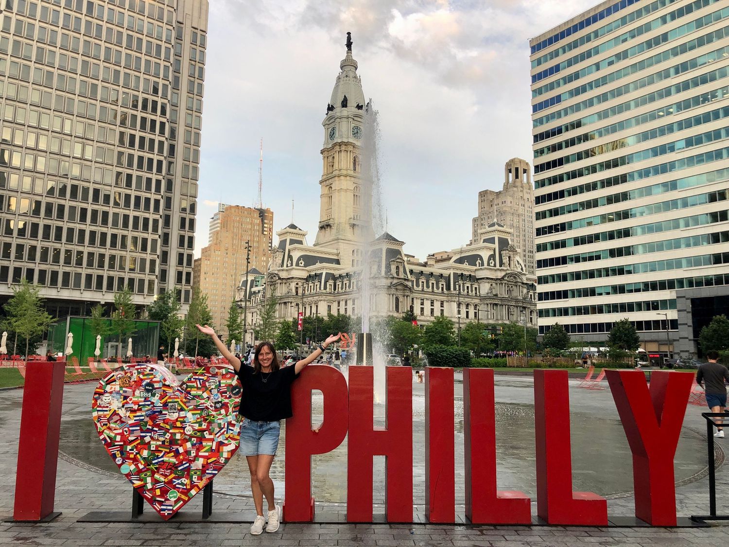Tourists posing in front of the iconic PHILLY sign with Philadelphia City Hall in the background.