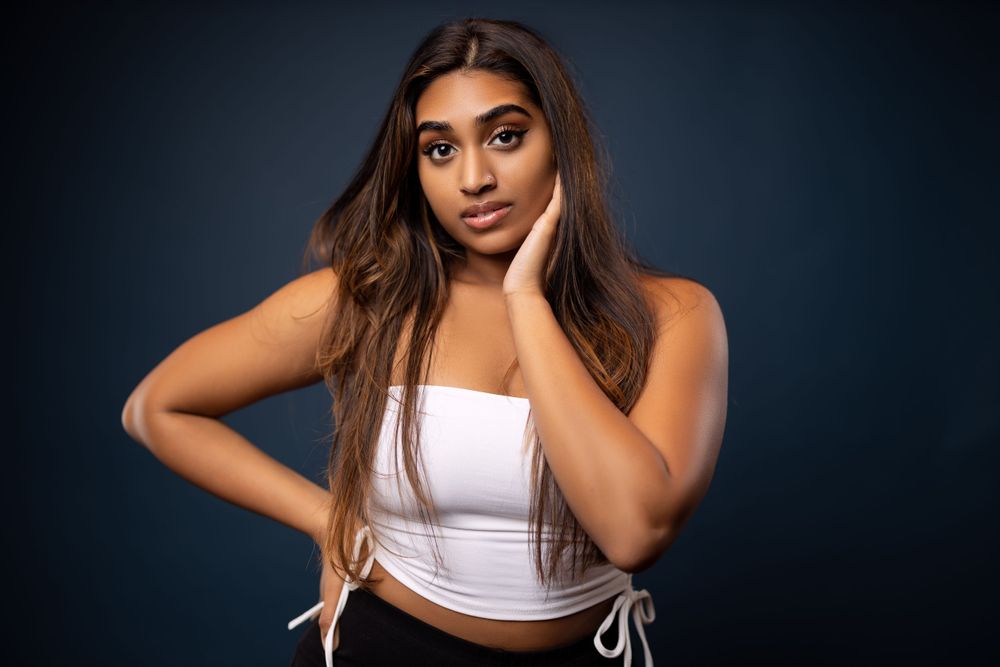 Model in white crop top poses with hand on neck against dark backdrop.