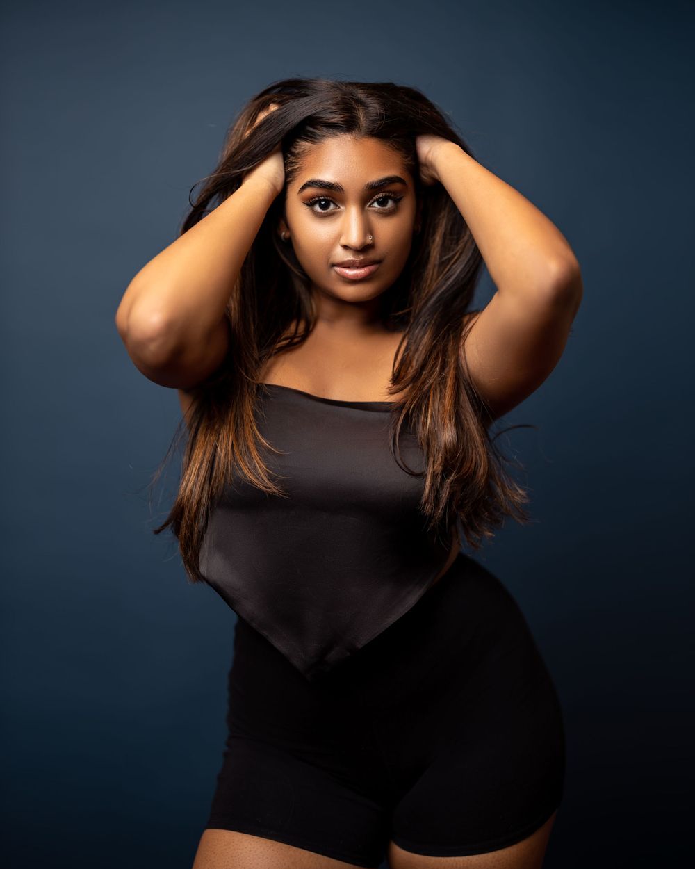 Model in black outfit poses with hands running through long hair.