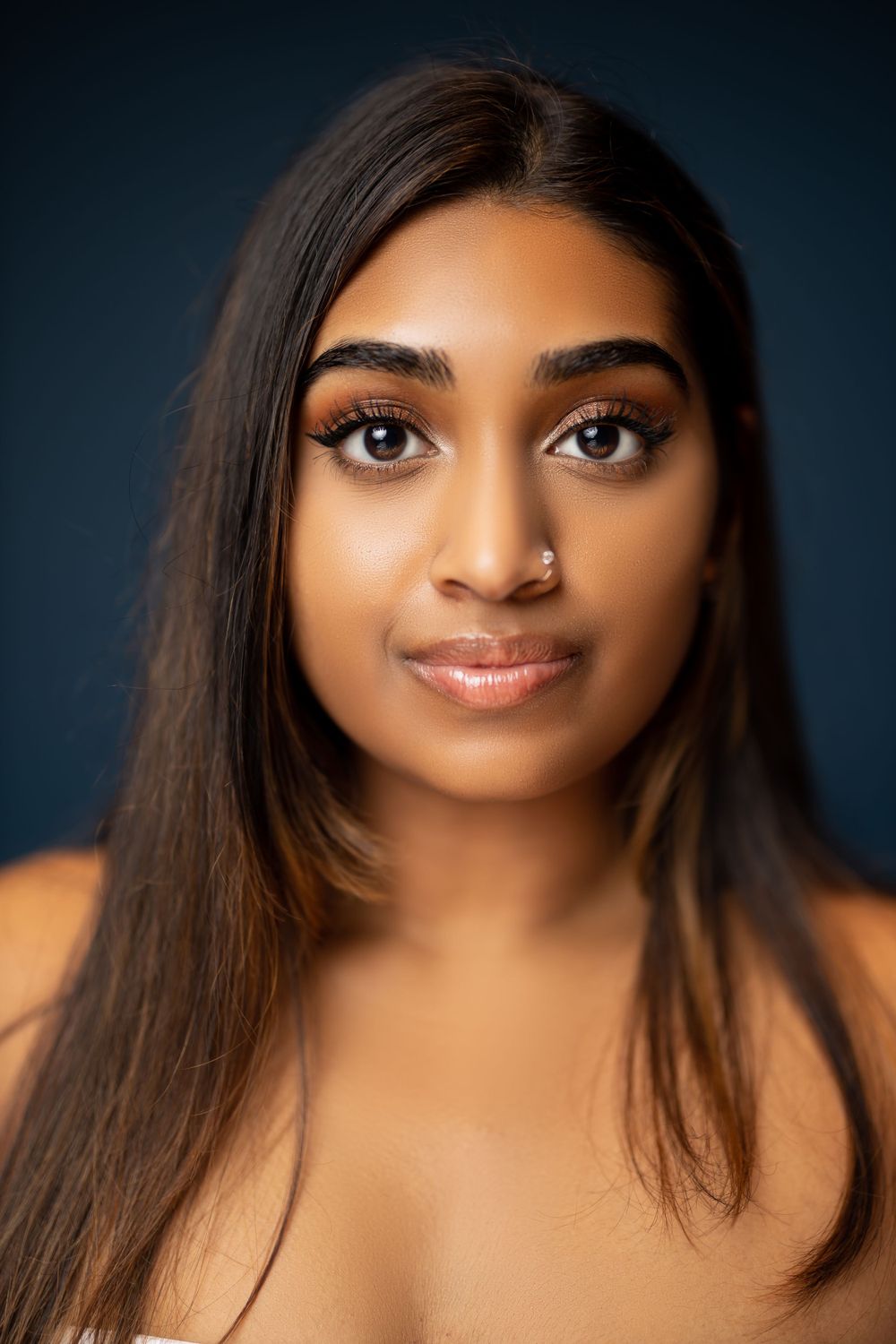 Beauty portrait showing glowing skin and natural makeup against dark blue background.