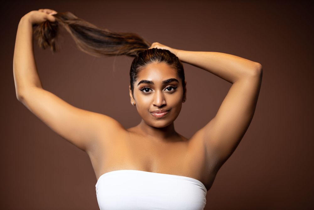 Model with long hair poses in white tube top against brown backdrop.