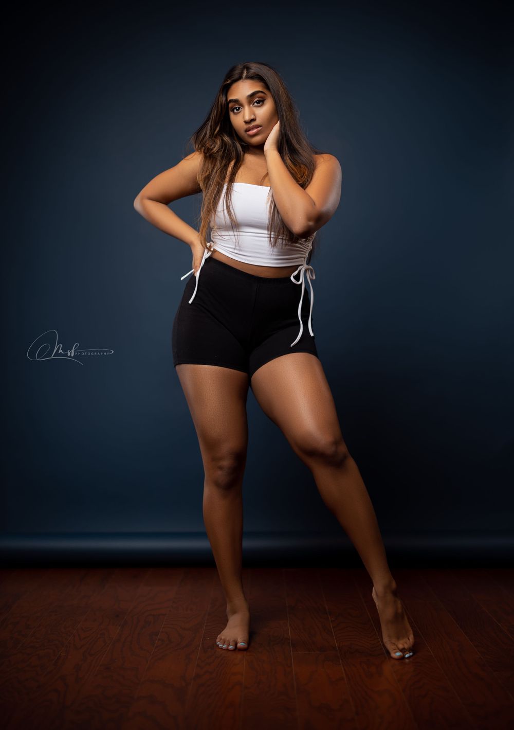 Model in white crop top and black shorts poses against dark studio backdrop.