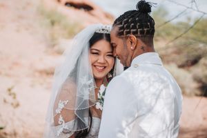 A tender moment between newlyweds in white attire against a desert landscape.