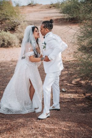 A romantic desert wedding photo of a couple in all white sharing a playful moment.