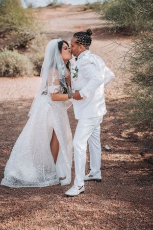 A passionate wedding kiss captured in a desert setting with natural foliage.