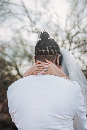 Back view of braided hairstyle with hands showing wedding rings and white veil outdoors.