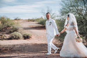 Couple walking hand in hand on desert trail in white wedding attire.
