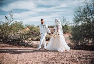 Wedding couple strolling along desert path in coordinated white outfits.