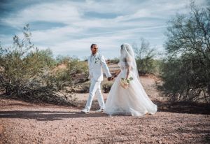 Newlyweds walking through desert landscape in matching white formal wear.