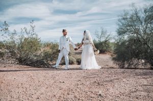 Newlyweds holding hands while walking on desert trail surrounded by desert vegetation.