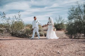 Couple in matching white outfits pose for wedding photos in desert landscape.