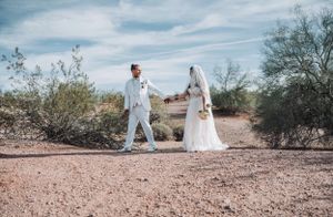 Wedding photo of couple in desert setting with cloudy blue sky backdrop.