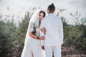 Tender moment between newlyweds in white against desert landscape backdrop.