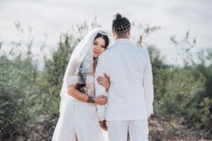 Romantic desert wedding portrait with couple embracing in all-white attire.
