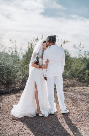 Intimate wedding moment captured in desert setting with desert brush and cloudy sky.